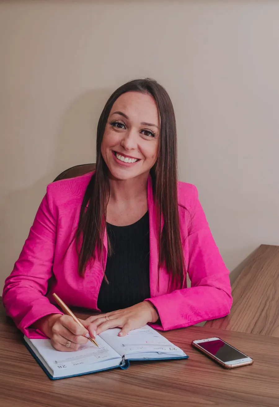 Dra. Ana Cristina Turos Laurindo, de blazer magenta, à mesa do escritório com uma agenda aberta