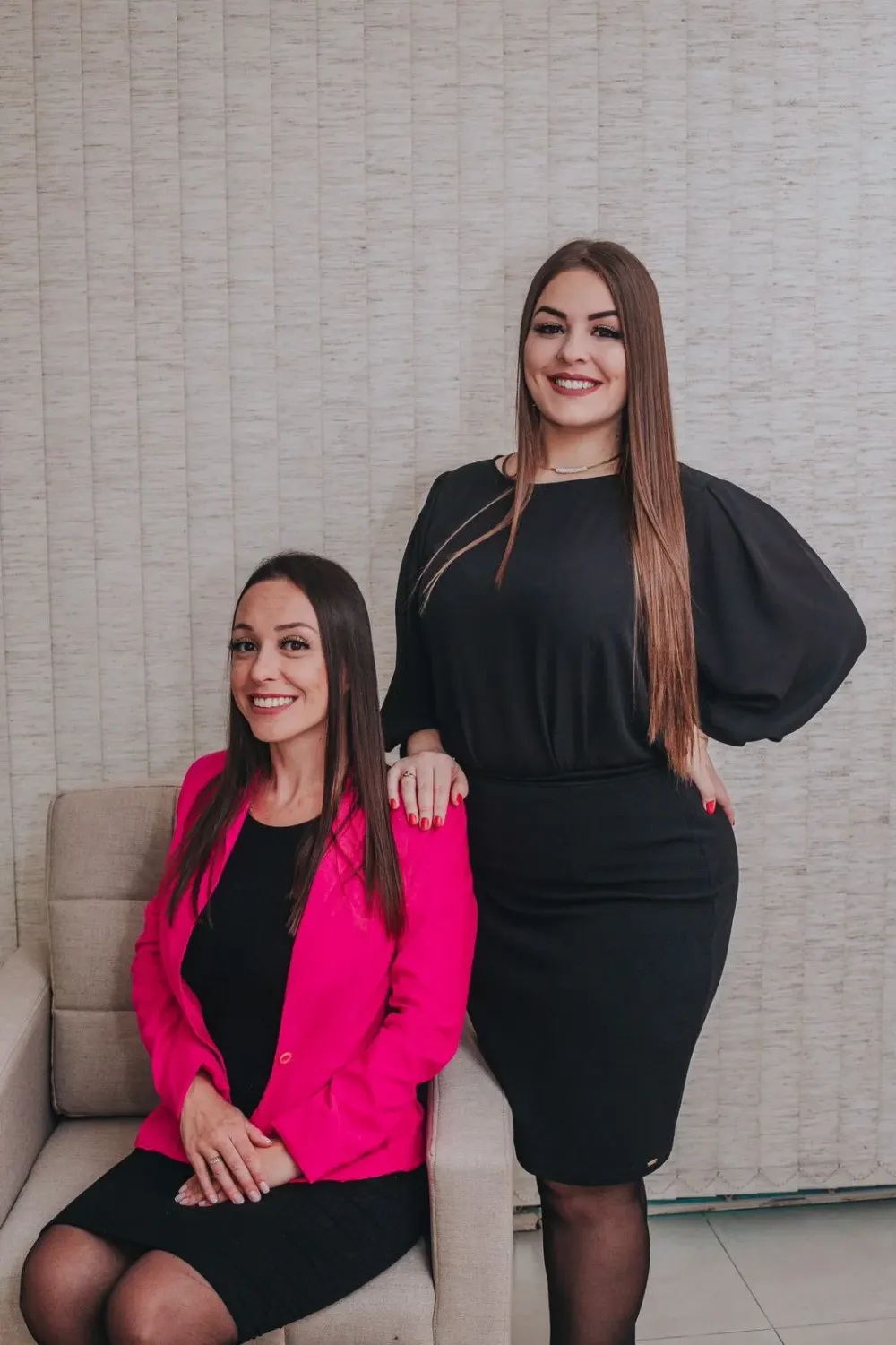 As sócias no escritório: Dra. Ana Cristina Turos Laurindo sentada, de blazer magenta, e Dra. Alana Maria Pezzini em pé, de vestido preto